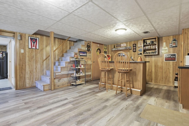 bar with wooden walls, wood finished floors, stairway, freestanding refrigerator, and a dry bar