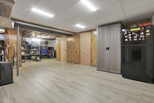 finished basement with a paneled ceiling, wooden walls, wood finished floors, and freestanding refrigerator