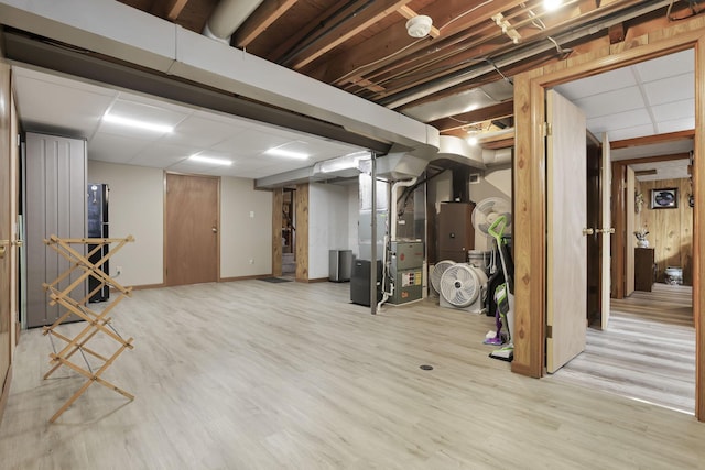 finished below grade area featuring light wood-type flooring, baseboards, a drop ceiling, and heating unit