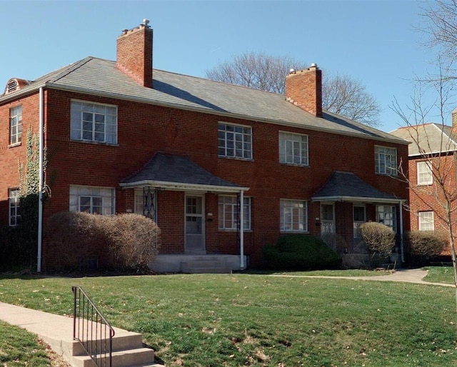 view of front of home featuring a front yard, a chimney, and brick siding