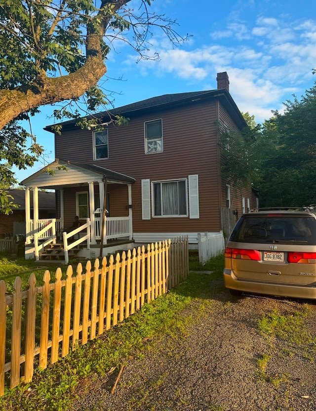 view of front of home featuring a fenced front yard, a chimney, and a porch