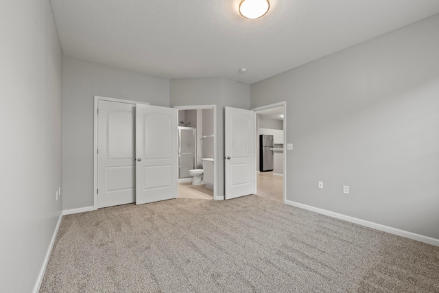 unfurnished bedroom featuring carpet, baseboards, ensuite bath, and freestanding refrigerator