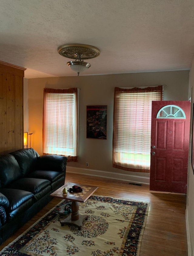 living room featuring visible vents, a textured ceiling, baseboards, and wood finished floors