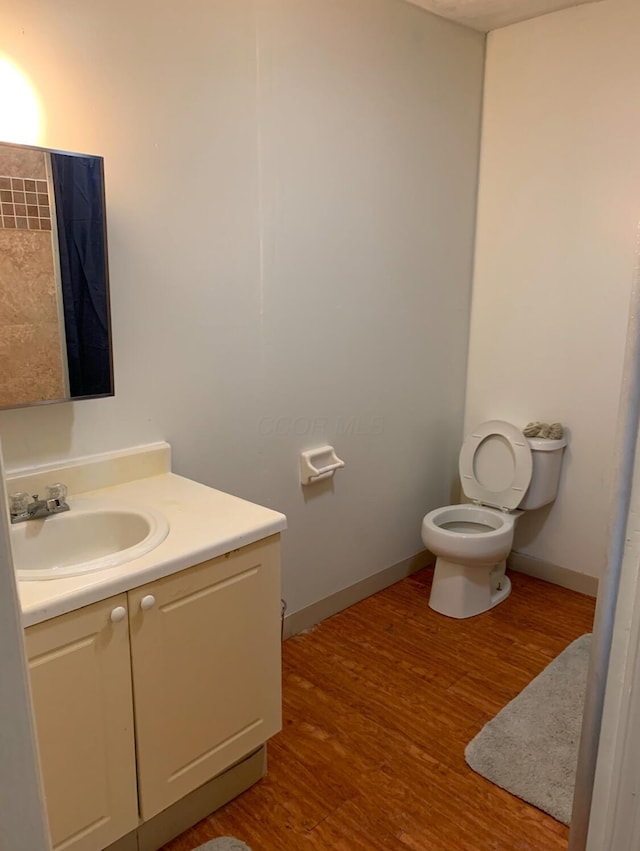 bathroom featuring toilet, baseboards, wood finished floors, and vanity