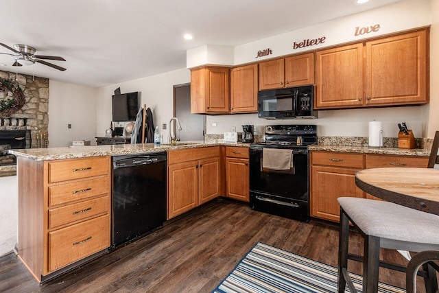 kitchen with light stone counters, a peninsula, a sink, dark wood-style floors, and black appliances