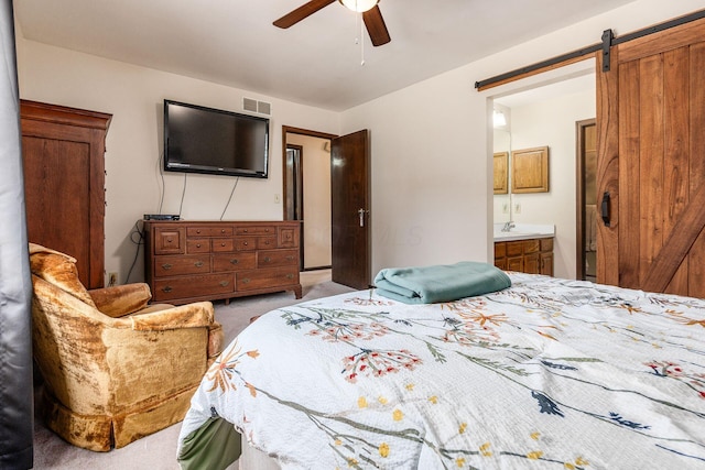 bedroom featuring a barn door, connected bathroom, light carpet, visible vents, and a ceiling fan