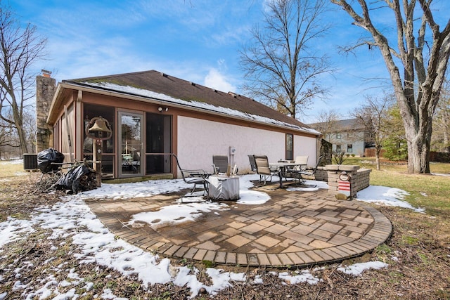 snow covered house featuring a chimney, outdoor dining area, cooling unit, a patio area, and stucco siding