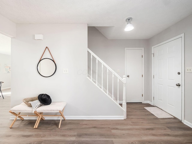 entrance foyer with baseboards, a textured ceiling, stairway, and wood finished floors