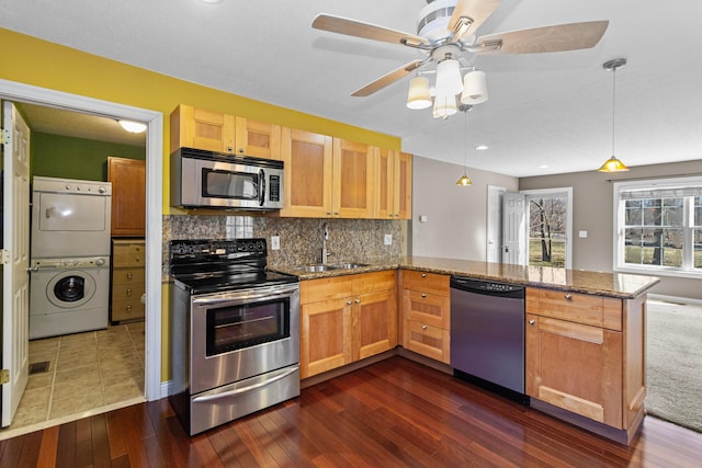 kitchen with stainless steel appliances, stacked washer / dryer, a peninsula, and dark stone countertops