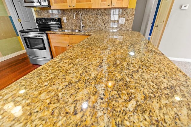 kitchen featuring stainless steel appliances, tasteful backsplash, brown cabinetry, a sink, and light stone countertops