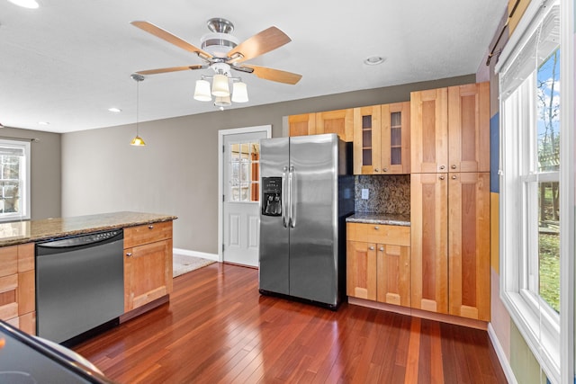 kitchen with tasteful backsplash, dark wood finished floors, glass insert cabinets, appliances with stainless steel finishes, and light stone counters