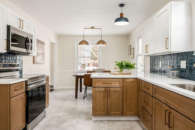 kitchen with light countertops, appliances with stainless steel finishes, decorative light fixtures, and white cabinets