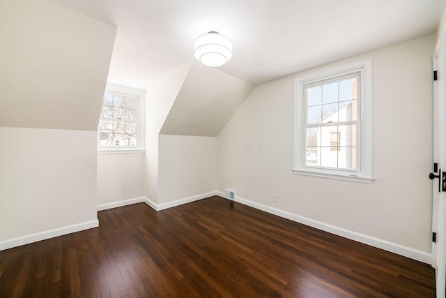 additional living space with dark wood-style floors, baseboards, visible vents, and vaulted ceiling