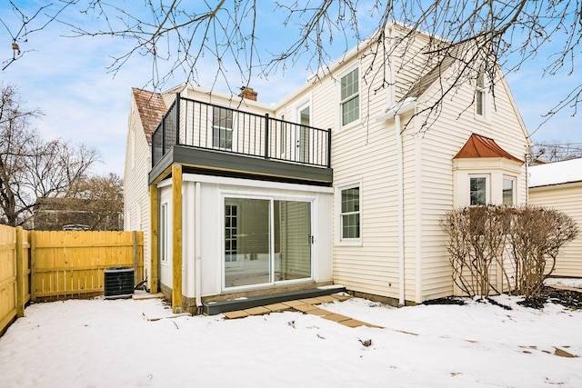 snow covered property featuring cooling unit, fence, and a balcony