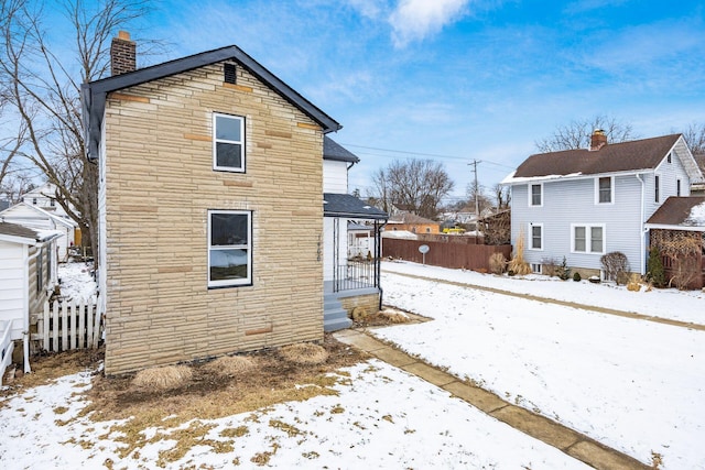 view of snowy exterior with stone siding, a chimney, and fence