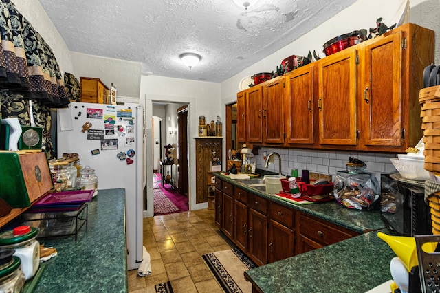 kitchen with tasteful backsplash, dark countertops, a sink, and freestanding refrigerator