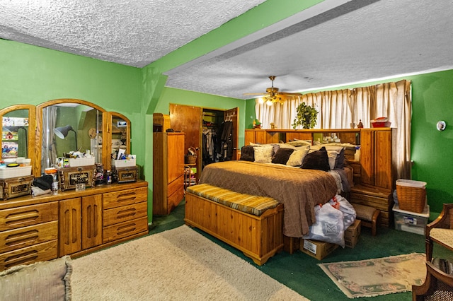 bedroom with a textured ceiling, ceiling fan, a closet, dark colored carpet, and a walk in closet