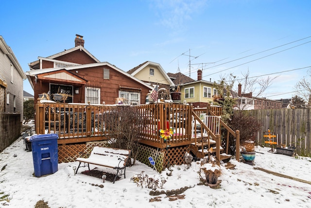 snow covered back of property featuring fence, a chimney, and a wooden deck