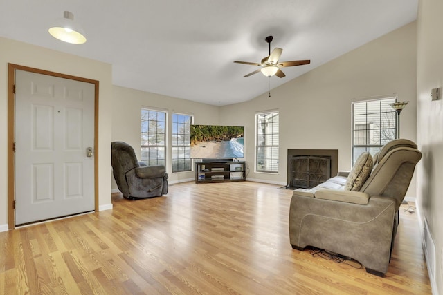 living area featuring lofted ceiling, a fireplace with flush hearth, a ceiling fan, baseboards, and light wood-style floors