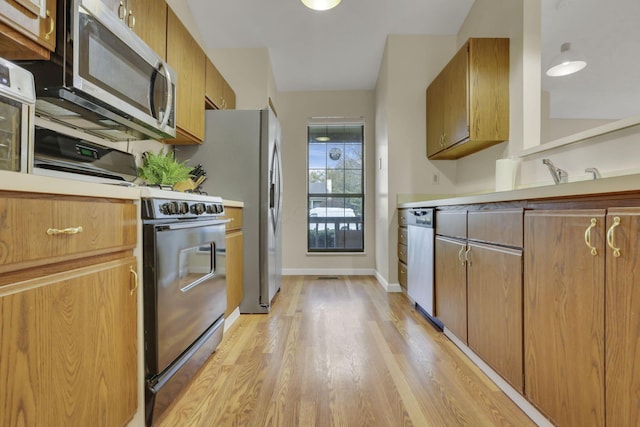 kitchen with baseboards, light wood-style floors, light countertops, appliances with stainless steel finishes, and brown cabinets