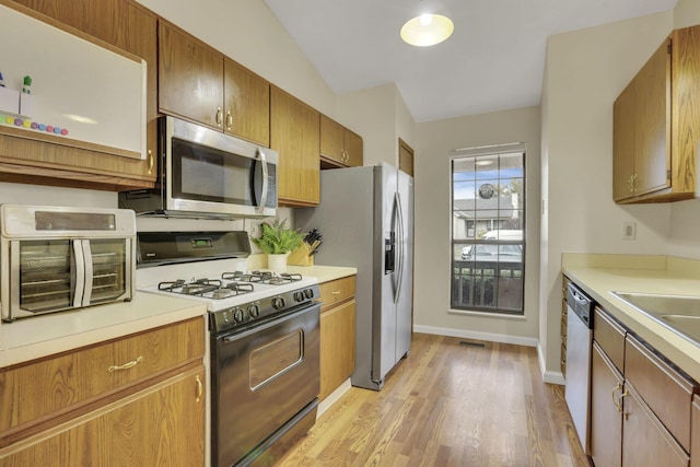 kitchen featuring a toaster, stainless steel appliances, light countertops, light wood-style flooring, and baseboards