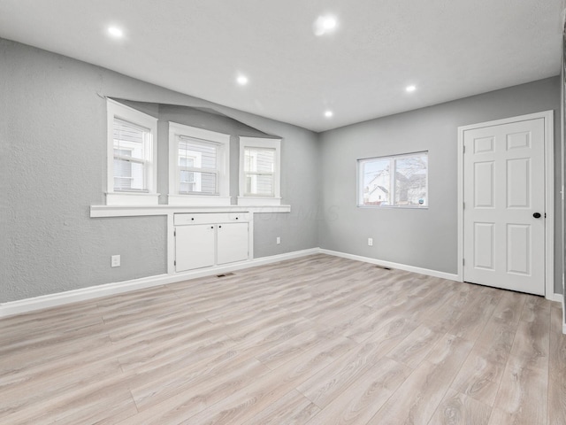 empty room featuring light wood-type flooring, a textured wall, baseboards, and recessed lighting