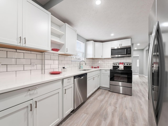 kitchen with light wood finished floors, stainless steel appliances, tasteful backsplash, light countertops, and a sink