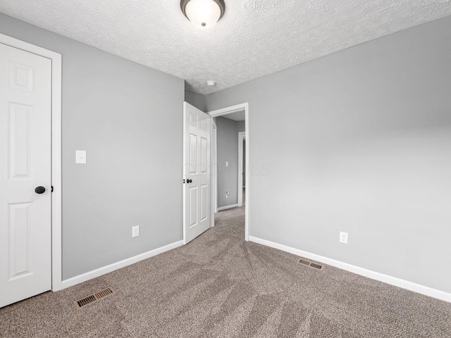 unfurnished bedroom with carpet floors, visible vents, a textured ceiling, and baseboards