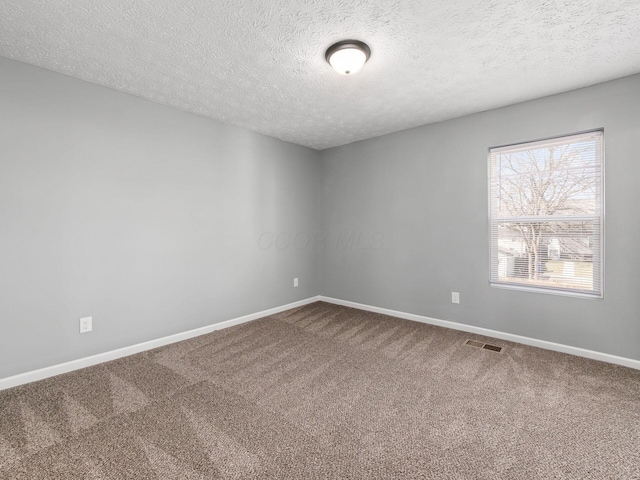 spare room featuring carpet floors, visible vents, a textured ceiling, and baseboards