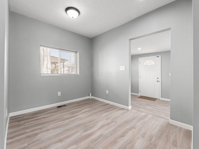 spare room featuring light wood finished floors, visible vents, baseboards, and a textured ceiling