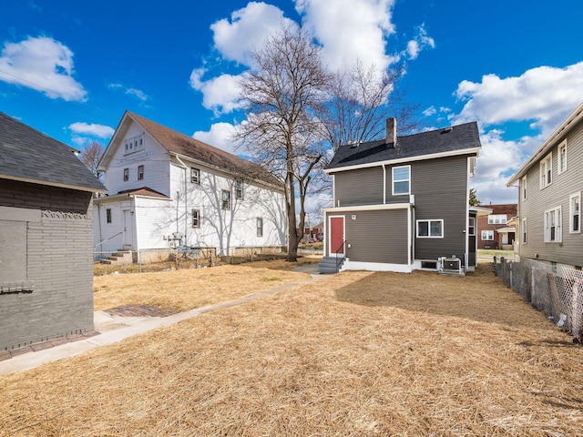 back of house featuring entry steps, a chimney, fence, and a lawn