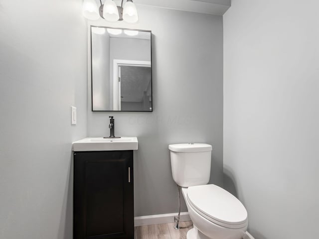 half bath with toilet, an inviting chandelier, vanity, wood finished floors, and baseboards