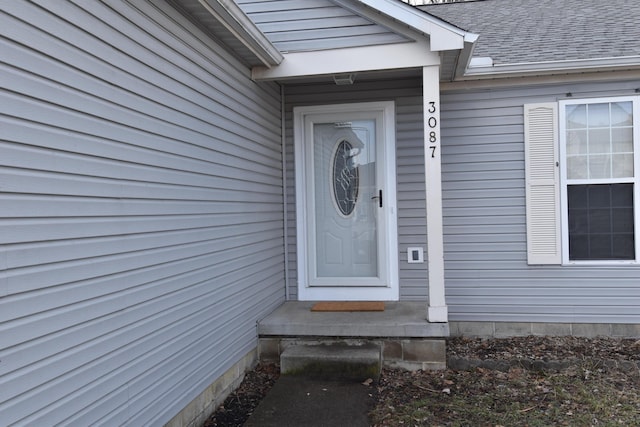 view of exterior entry with roof with shingles