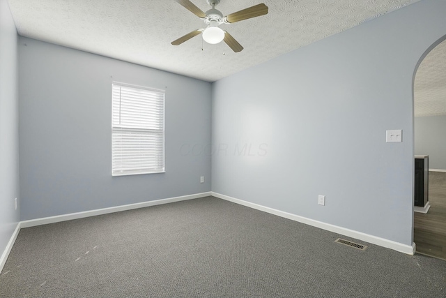 spare room featuring arched walkways, dark colored carpet, ceiling fan, a textured ceiling, and baseboards