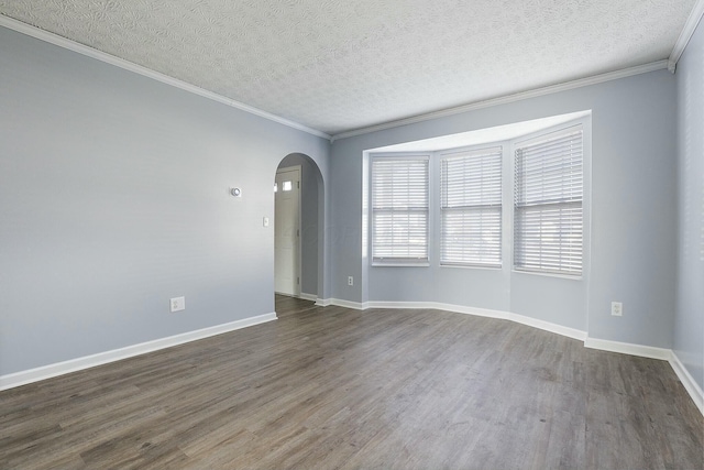 spare room with arched walkways, dark wood-style flooring, crown molding, and baseboards