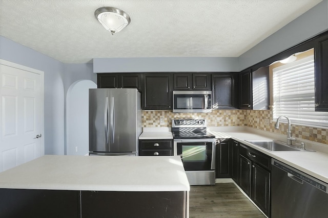 kitchen featuring stainless steel appliances, light countertops, decorative backsplash, dark wood-type flooring, and a sink