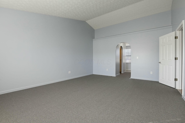 unfurnished bedroom featuring baseboards, arched walkways, vaulted ceiling, a textured ceiling, and dark colored carpet