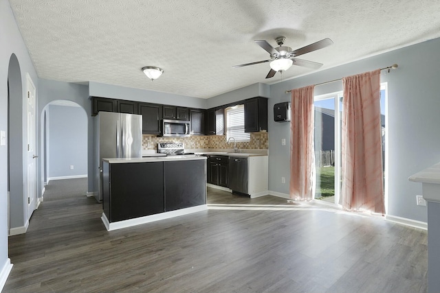 kitchen with arched walkways, stainless steel appliances, light countertops, a center island, and tasteful backsplash