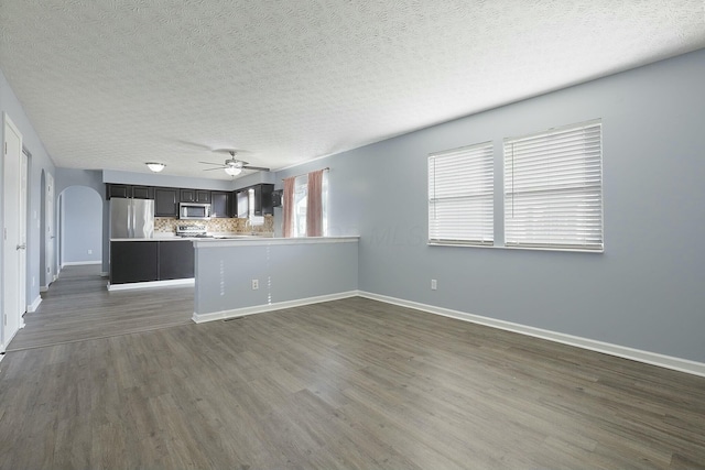 unfurnished living room featuring dark wood-style floors, baseboards, arched walkways, and a textured ceiling