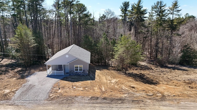 view of front of property featuring covered porch, stone siding, gravel driveway, and a view of trees