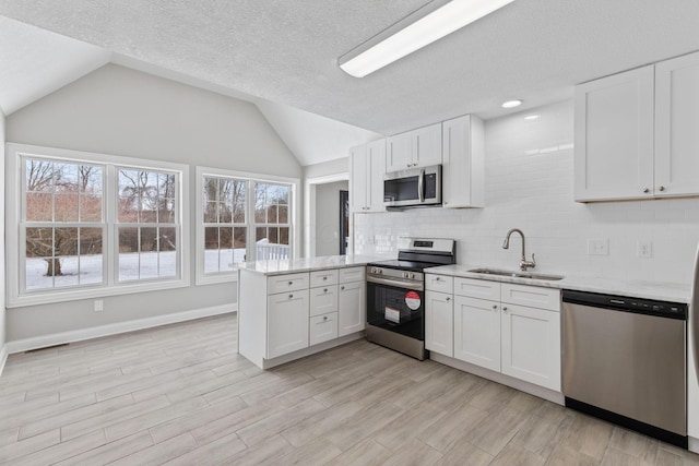 kitchen with a peninsula, appliances with stainless steel finishes, a sink, and white cabinetry