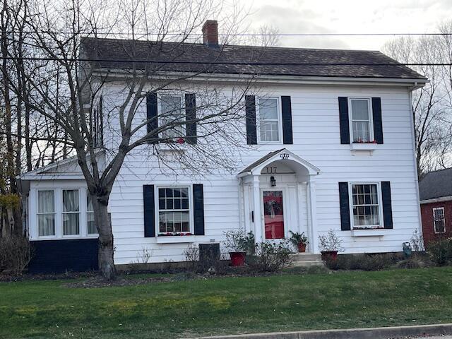 colonial home featuring a shingled roof, a front yard, and a chimney