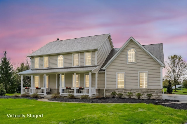 view of front of property with a porch, stone siding, and a yard