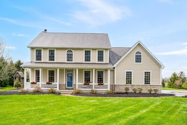 colonial home with a porch, stone siding, roof with shingles, and a front yard