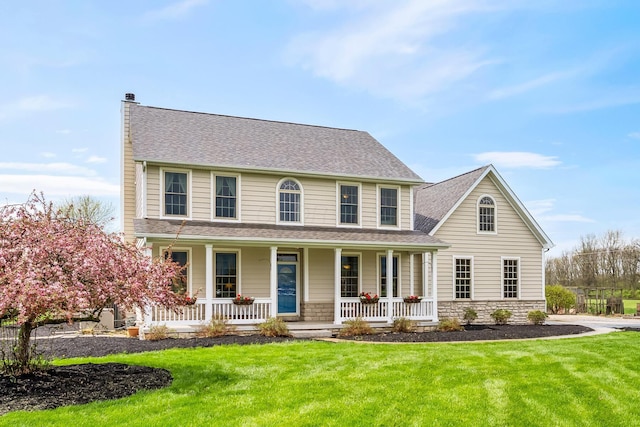 colonial home featuring roof with shingles, a front lawn, stone siding, a chimney, and covered porch