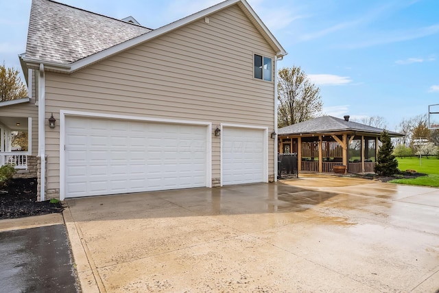 view of home's exterior with a garage, roof with shingles, a gazebo, and concrete driveway