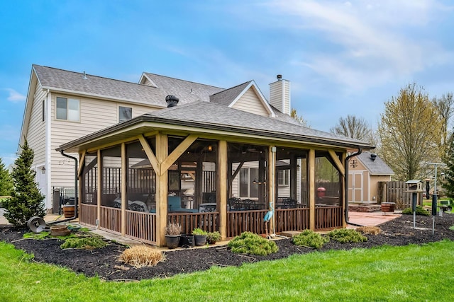 back of property with a yard, a sunroom, a shingled roof, and a chimney