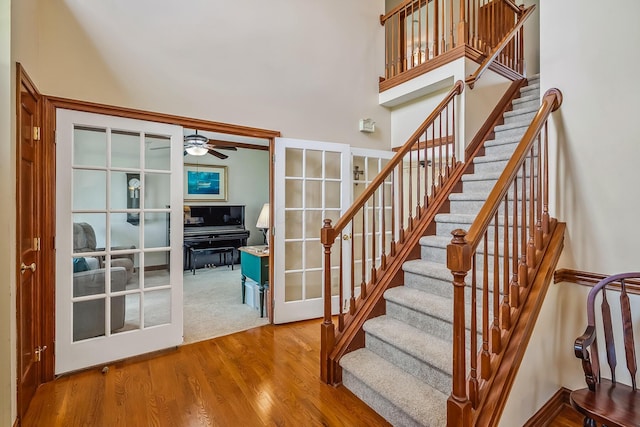 staircase with a towering ceiling, french doors, wood finished floors, and ceiling fan