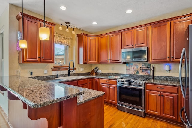 kitchen featuring stainless steel appliances, a peninsula, light wood-style flooring, a sink, and decorative light fixtures