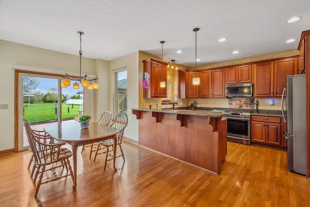 kitchen with a kitchen breakfast bar, stainless steel appliances, light wood-style flooring, a peninsula, and a notable chandelier